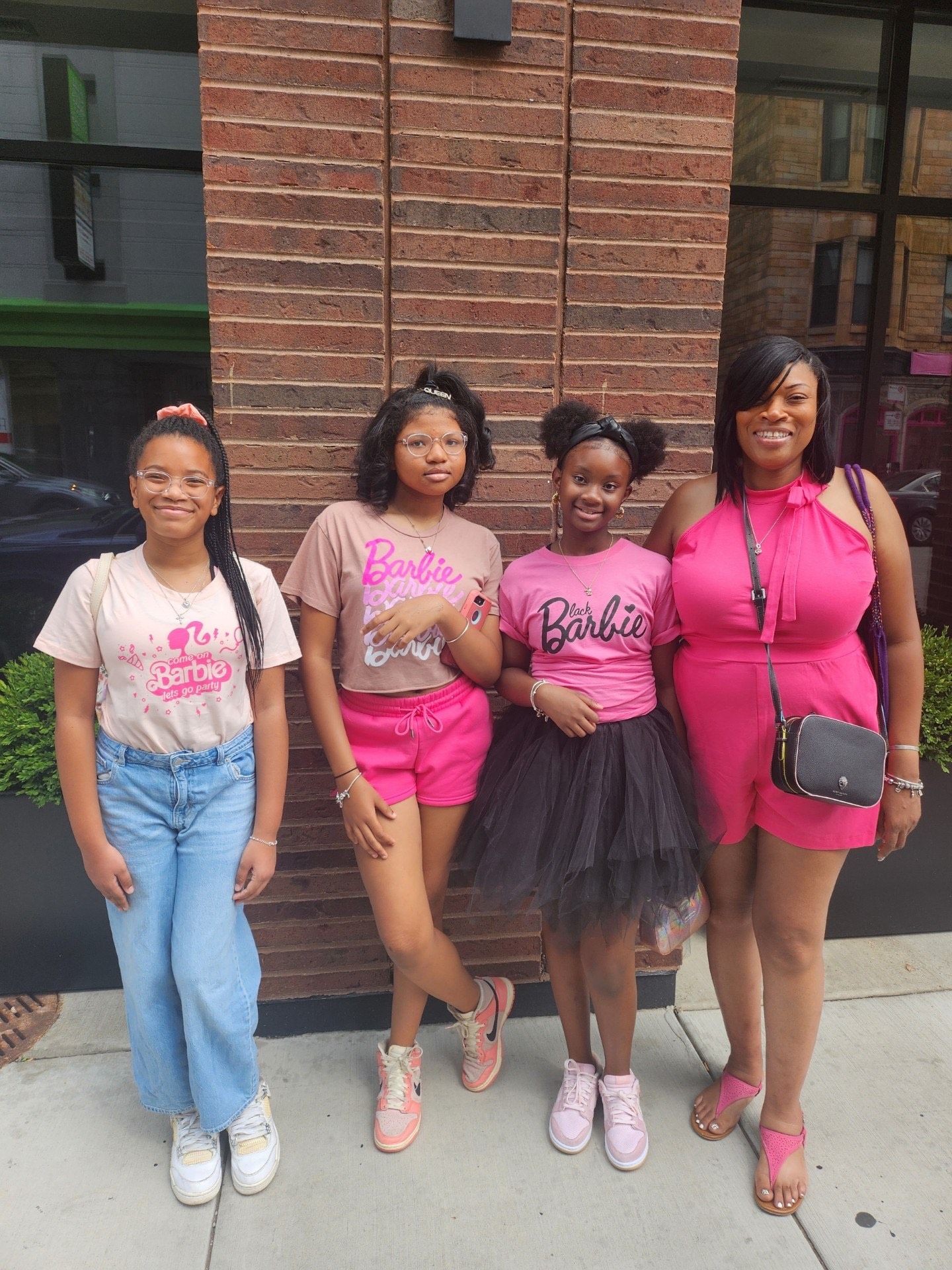 Four people wearing pink-themed outfits posing in front of a brick wall.