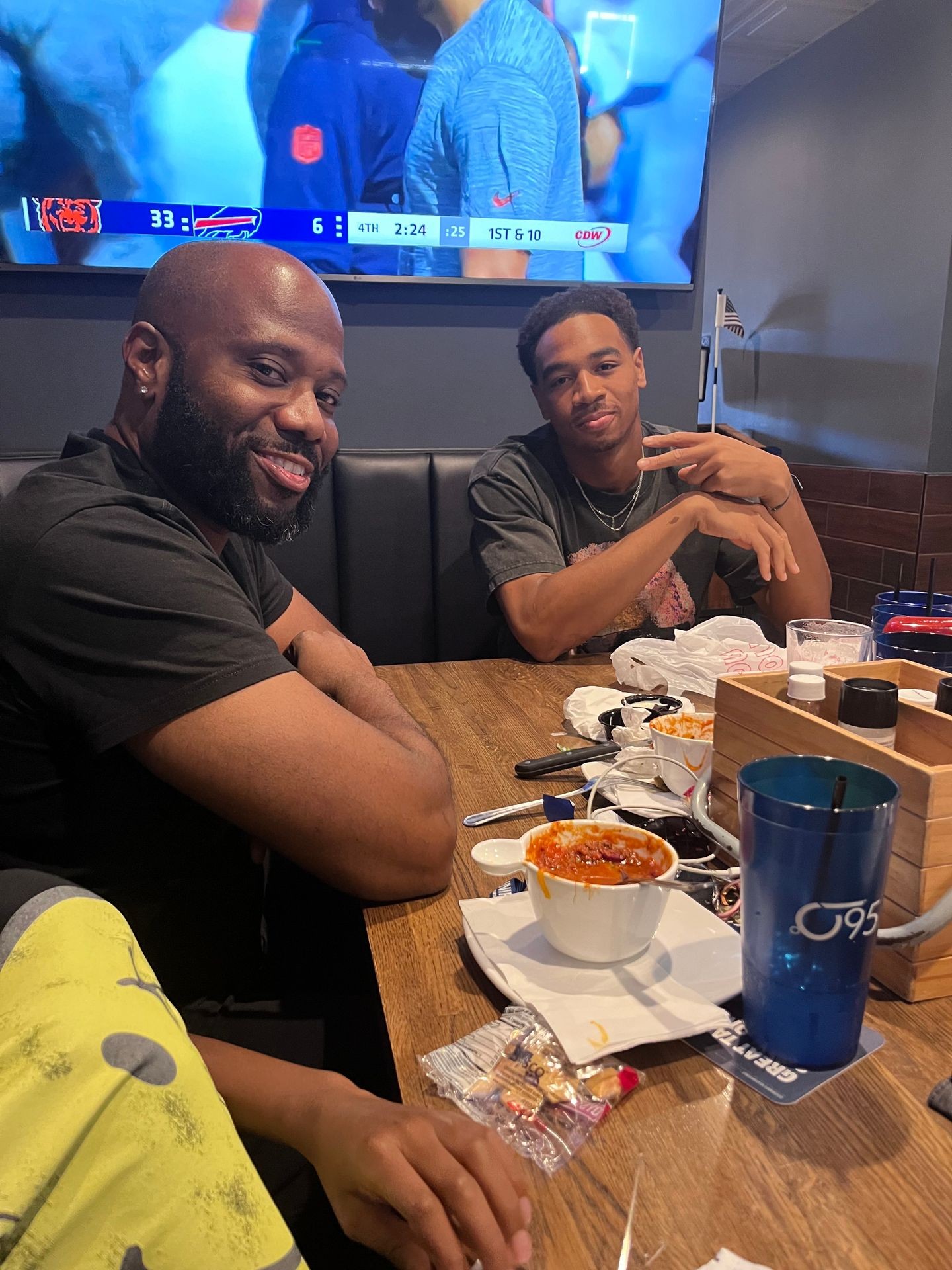 Two people sitting at a table in a restaurant with a football game on TV in the background.